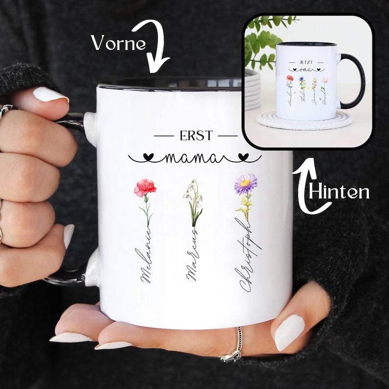 May include: White ceramic mug with a black interior and handle, featuring the text "ERST mama" and floral illustrations. The names Melanie, Marcus, and Christoph are written below the flowers. A smaller mug with similar design is in the background.