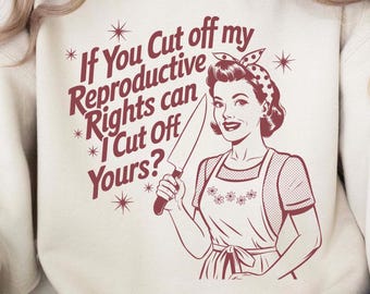 May include: Cream-colored sweatshirt with a retro-style illustration and text. The graphic features a woman holding a knife, accompanied by the phrase, "If You Cut off my Reproductive Rights can I Cut Off Yours?"