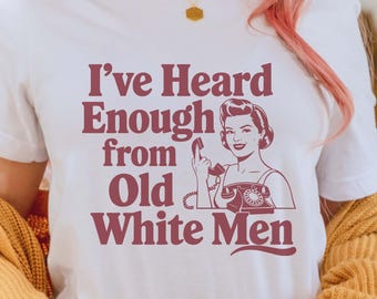 May include: White t-shirt with a red graphic that says "I've Heard Enough from Old White Men". The graphic features a woman on the phone with a finger to her lips.