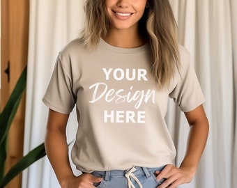 May include: A woman wearing a light beige t-shirt with the text "YOUR Design HERE" printed on the front. She is standing in front of a white curtain.
