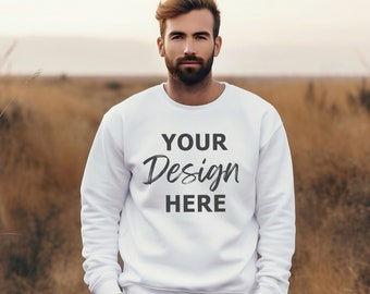 May include: A white crew neck sweatshirt with the text "YOUR Design HERE" in black. The sweatshirt is worn by a person standing in a field of tall grass. The person is wearing gray pants and has their hands in their pockets.