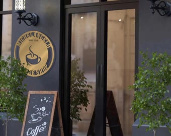 Pode incluir: Uma fachada de loja em preto fosco com dois candeeiros de parede pretos e um letreiro circular dourado com a inscrição Michelangelo Coffee Shop Since 2015. Um cavalete de madeira exibe desenhos de café em giz branco e o texto Coffee Served Here.