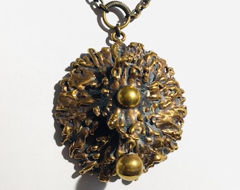 May include: A vintage-style pendant necklace featuring a textured, bronze-colored pendant with two gold-colored spheres. The pendant hangs from a matching bronze chain. The design has an organic, almost floral appearance.