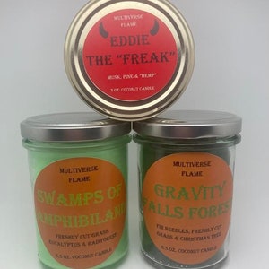 Könnte beinhalten: Drei Glas-Kerzenbehälter mit Metalldeckeln. Die Deckel sind mit dem Text "MULTIVERSE FLAME" und den Namen der Düfte beschriftet: "EDDIE THE "FREAK" - MOSCHUS, KIEFER & "HANF" - 3 OZ. KOKOSNUSS-KERZE", "SWAMPS OF AMPHIBILAND - FRISCH GESCHNITTENES GRAS, EUKALYPTUS & REGENWALD - 6,5 OZ. KOKOSNUSS-KERZE", und "GRAVITY FALLS FOREST - TANNENNADELN, FRISCH GESCHNITTENES GRAS & WEIHNACHTSBAUM - 6,5 OZ. KOKOSNUSS-KERZE".