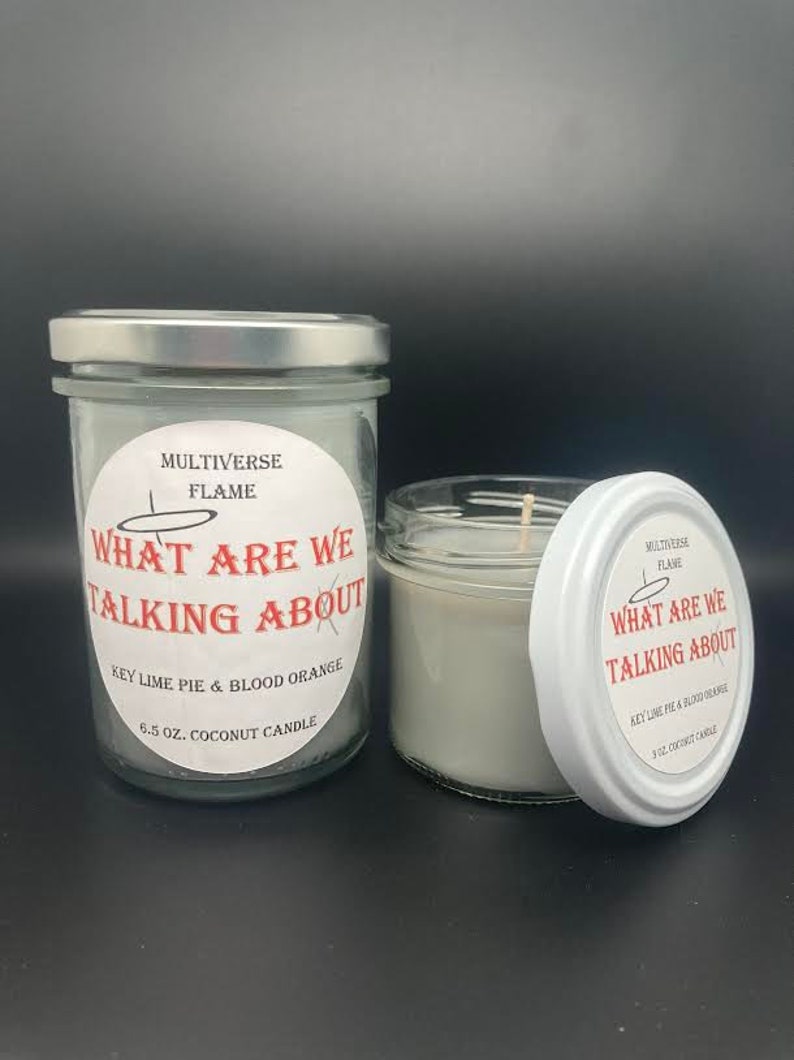May include: Two glass jars with white lids and labels. The labels are white with black text and a red circle that says "What are we talking about". The text on the labels says "Multiverse Flame" and "Key Lime Pie & Blood Orange 6.5 oz. Coconut Candle".