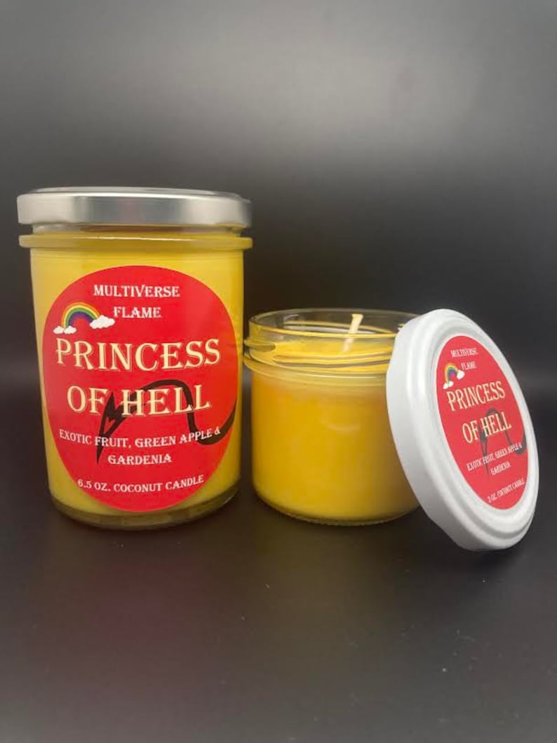 May include: Two yellow coconut candles in glass jars with silver lids. The labels are red with black text and a rainbow graphic. The text on the labels reads "MULTIVERSE FLAME PRINCESS OF HELL EXOTIC FRUIT, GREEN APPLE & GARDENIA 6.5 OZ. COCONUT CANDLE".