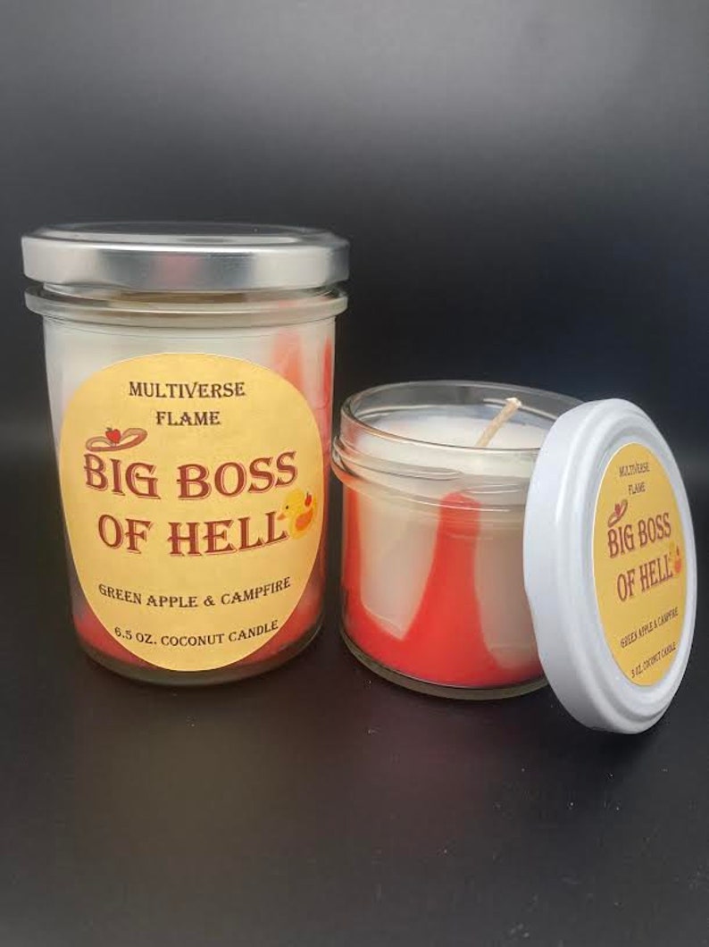 May include: Two glass jars with red and white wax candles. The jars have labels that say "MULTIVERSE FLAME BIG BOSS OF HELL GREEN APPLE & CAMPFIRE 6.5 OZ. COCONUT CANDLE".