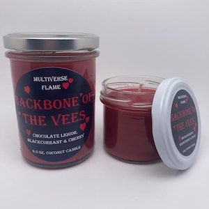 May include: Two red glass jars with silver lids. The jars contain red wax and a wick. The jars have a label that reads "MULTIVERSE FLAME BACKBONE OF THE VEES CHOCOLATE LIQUOR BLACKCURRANT & CHERRY 6.5 OZ. COCONUT CANDLE".