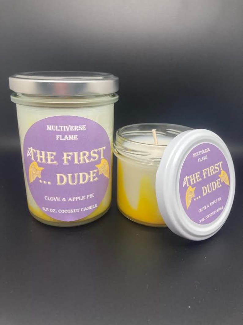 May include: Two glass jars with lids containing coconut candles. The jars have purple labels with the text "MULTIVERSE FLAME THE FIRST...DUDE CLOVE & APPLE PIE 6.5 OZ. COCONUT CANDLE" and "MULTIVERSE FLAME THE FIRST...DUDE CLOVE & APPLE PIE 3 OZ. COCONUT CANDLE".