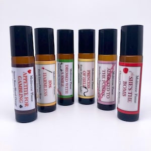 Può includere: Un set di dieci flaconi di vetro da 10 ml con tappi neri. Ogni flacone ha un'etichetta diversa con un nome e una descrizione del profumo unici. Le etichette sono colorate e presentano vari disegni, tra cui cuori, un serpente, una ciliegia e una carta da gioco. I flaconi sono disposti in fila su una superficie bianca.