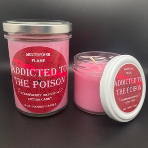 May include: Two pink glass jars with silver lids. The jars contain a pink candle and have a red and white label that reads "Addicted to the Poison" with the scent "Strawberry Daiquiri & Cotton Candy". The label also says "3 oz. Coconut Candle" and "Multiverse Flame".