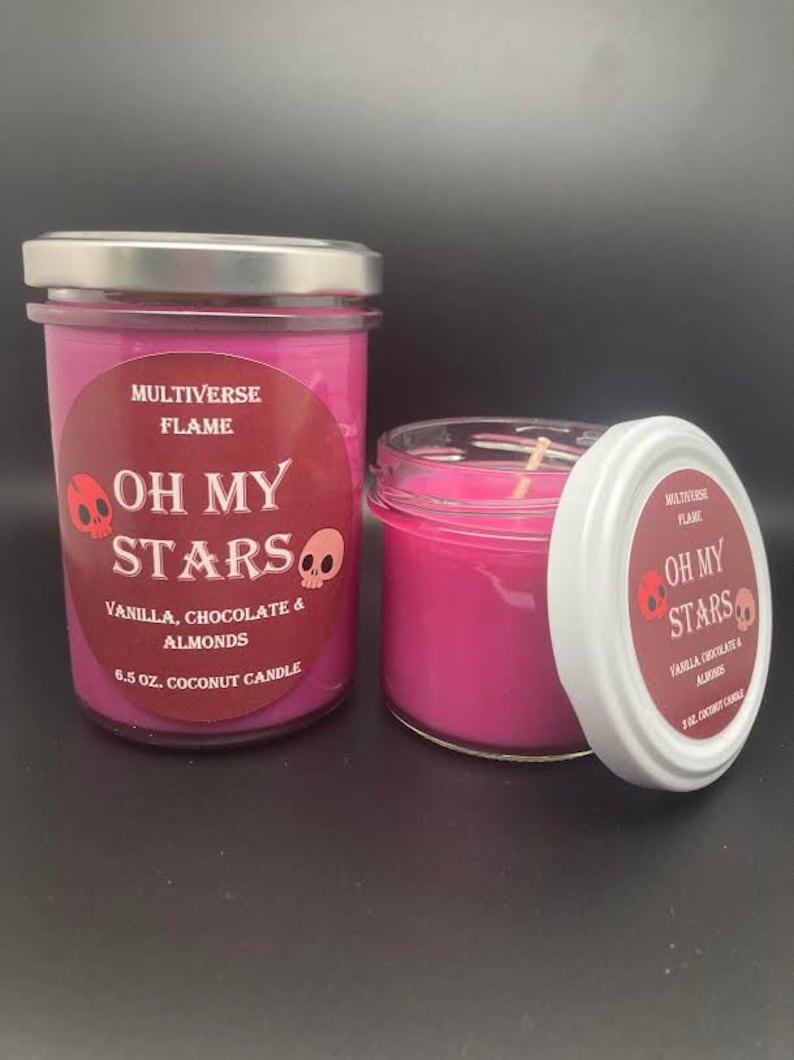 May include: Two pink coconut wax candles with a skull and crossbones design and the text "Oh My Stars" on the label. The candles are labeled "Vanilla, Chocolate & Almonds" and are 6.5 oz.