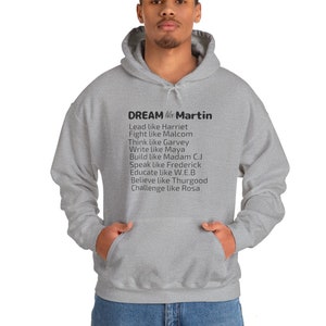 Peut inclure: Un sweat à capuche gris avec le texte "DREAM like Martin" et une liste de noms et d'actions, notamment "Lead like Harriet", "Fight like Malcom", "Think like Garvey", "Write like Maya", "Build like Madam C.J", "Speak like Frederick", "Educate like W.E.B", "Believe like Thurgood", et "Challenge like Rosa".