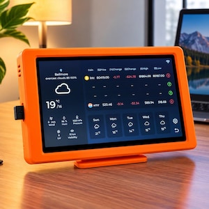 May include: A bright orange digital display device featuring a screen that shows weather information, including temperature, wind speed, and humidity, alongside cryptocurrency market data. The screen displays the text Bellmore and Good Ideas Better Days.