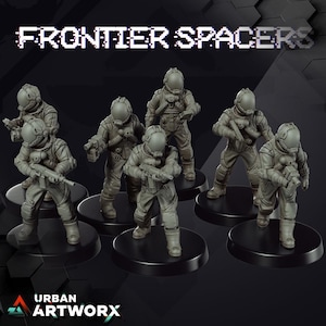 Op de afbeelding: Een verzameling grijze miniatuurfiguren van ruimteverkenners, elk met een helm en uniform, die wapens vasthouden. De figuren staan op zwarte, cirkelvormige bases. De tekst "FRONTIER SPACERS" staat bovenaan. Het Urban Artworx-logo staat onderaan.