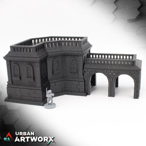 Könnte beinhalten: Ein graues, 3D-gedrucktes Gebäude mit einem Balkon und einem Bogenportal. Das Gebäude hat eine strukturierte Oberfläche und ist aus robustem Material gefertigt.