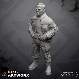 Può includere: Una miniatura stampata in 3D di colore grigio di una persona che indossa una giacca e pantaloni. La persona ha i capelli corti e grigi e un'espressione seria.