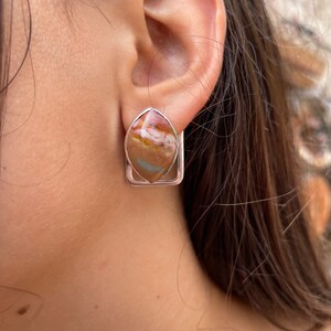 May include: A pair of silver earrings with a brown, white, and blue agate stone set in a geometric frame.