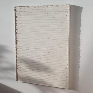 Può includere: Arte da parete bianco testurizzato con linee orizzontali. Le linee sono in rilievo e creano un effetto tridimensionale.
