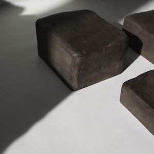 K&ouml;nnte beinhalten: Drei dunkelbraune Holzbl&ouml;cke, jeder mit einer quadratischen Form und einer rauen, strukturierten Oberfl&auml;che.