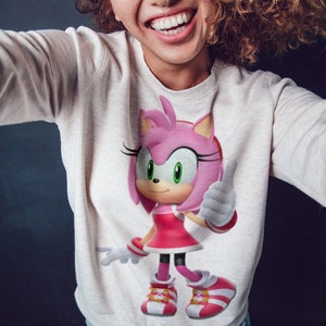 May include: A white sweatshirt with a pink and white cartoon character wearing a red dress and white shoes. The character is giving a thumbs up.