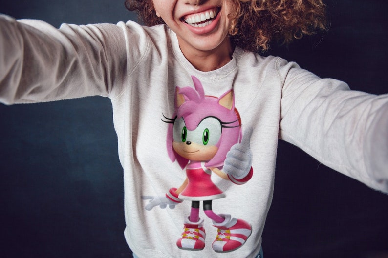 May include: A white sweatshirt with a pink and white cartoon character wearing a red dress and white shoes. The character is giving a thumbs up.