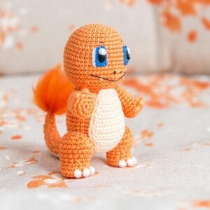 May include: A crocheted orange and white plush toy resembling a cartoon character with a tail. The toy has blue eyes and a smiling expression.