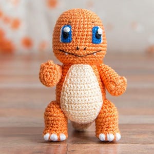 May include: A crocheted orange and white plush toy resembling a cartoon character with blue eyes. The toy has a small mouth and a tail.