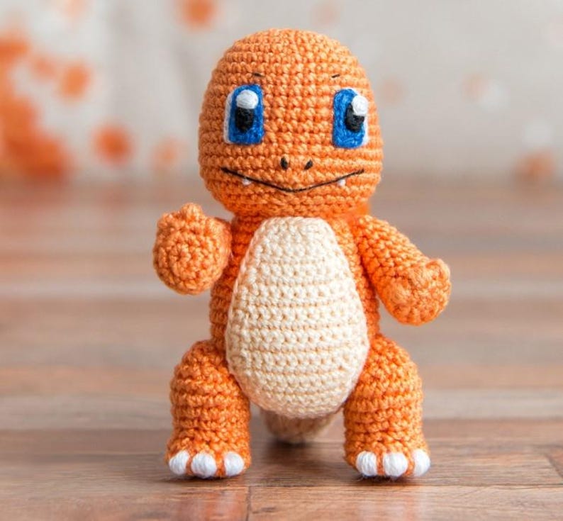 May include: A crocheted orange and white plush toy resembling a cartoon character with blue eyes. The toy has a small mouth and a tail.