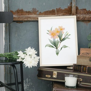 May include: A framed watercolor print featuring a floral arrangement with yellow and pink blossoms and green leaves. The artwork is displayed on a white background. The image also includes a black stool, white flowers, and vintage suitcases.