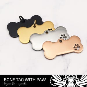 May include: Bone-shaped pet tags in black, gold, silver, and rose gold. Each tag has a paw print design and a loop for attaching to a collar. The text "BONE TAG WITH PAW" is visible at the bottom.