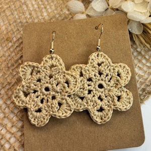 Op de afbeelding: Een paar gehaakte bloemoorbellen in beige met gouden haakjes. De oorbellen worden gepresenteerd op een bruine kaart met de tekst "FRANKY'S crochet ♥ patterns".