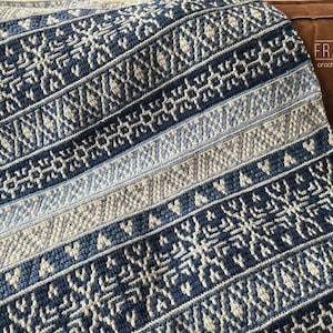 Op de afbeelding: Een blauwe en witte gehaakte deken met een geometrisch patroon. De deken is gemaakt met verschillende steken en texturen, wat een uniek en interessant ontwerp creëert.