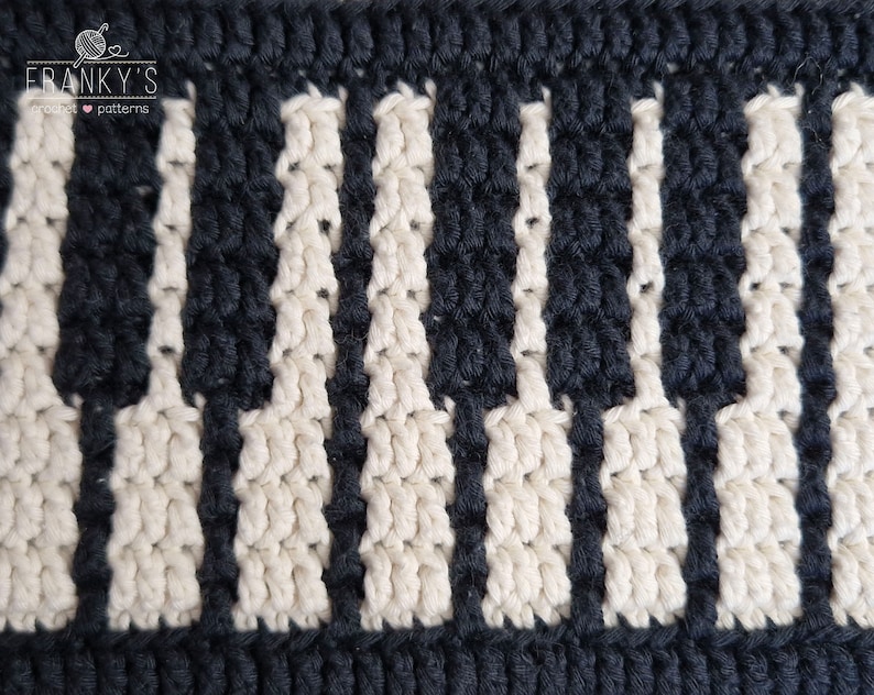 May include: Close-up of a crocheted piano keyboard pattern in black and white yarn. The pattern is made with a series of vertical stripes, creating the look of piano keys.
