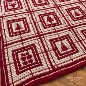 Op de afbeelding: Een handgemaakte, rood en crèmekleurige gehaakte deken met een kerstthema. De deken heeft een ruitpatroon met vierkanten met feestelijke symbolen zoals kerstbomen, bellen en cadeaus. De deken is gemaakt van zacht garen en heeft een decoratieve rand.