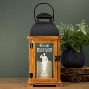 May include: A wooden lantern with a black top and handle. The front glass panel features the text "FORGE ENTER A TRAINEE LEAVE A SOLDIER" and a silhouette of a saluting soldier. The name "HUGHES" is below the soldier.