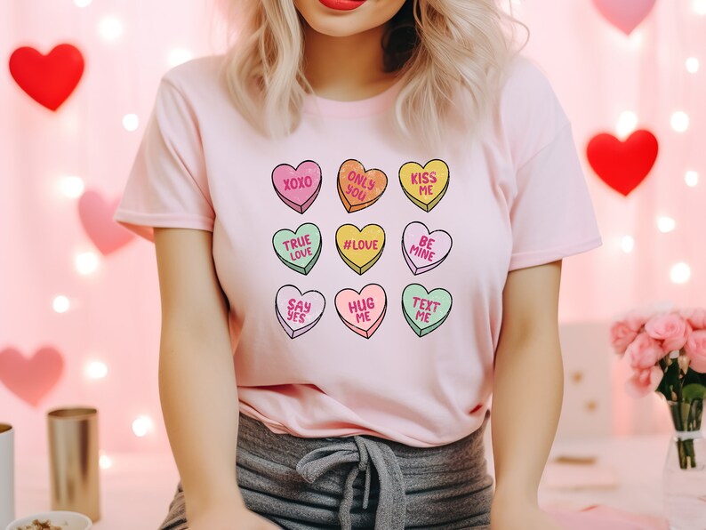 Pu&ograve; includere: Maglietta rosa con una grafica di nove cuori di caramelle con messaggi diversi, tra cui "XOXO", "True Love", "#Love", "Hug Me", "Say Yes", "Only You", "Kiss Me", "Be Mine" e "Text Me".