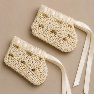 May include: Two ivory-colored, crocheted lace cuffs with floral patterns and satin ribbon accents. Each cuff has a rectangular shape with a scalloped edge and long, flowing ribbons.