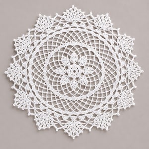 Peut inclure: Un napperon en crochet blanc de forme circulaire présentant un motif floral central entouré d'anneaux concentriques complexes en mailles ajourées et d'un bord festonné décoratif avec des motifs en forme de feuilles pointues.