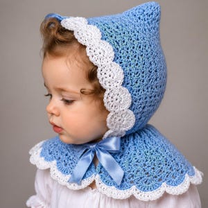 Peut inclure: Un bonnet en crochet bleu clair avec un sommet pointu et une bordure en dentelle blanche festonnée. Le bonnet est doté d'un ruban en satin bleu clair assorti au niveau du cou, offrant un ajustement sûr avec un détail de nœud décoratif.