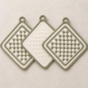 May include: Three square crochet potholders featuring a textured checkerboard pattern in sage green and off-white. Two potholders display a repeating grid of raised stitches, while the centre one features a solid off-white textured stitch. Each has a small loop.