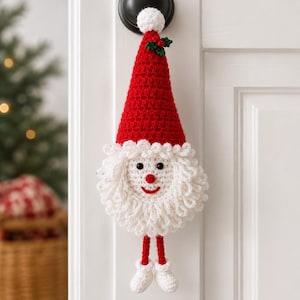 May include: A crocheted Santa Claus ornament featuring a tall red pointed hat with a white pom-pom and green holly leaves, a white curly beard, a round red nose, a stitched red smile, and two dangling red legs with white boots.