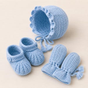 May include: A light blue crochet set consisting of a bonnet with a ruffled edge and two ties, a pair of booties with side buttons, and a pair of mittens with drawstring ties. Each item is crafted from yarn in a consistent light blue shade.