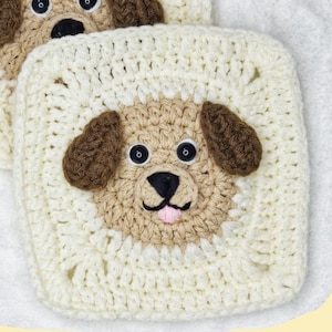 Puede incluir: Un cuadrado de crochet con un perro marrón y beige con ojos negros y lengua rosa. El perro está rodeado de un borde blanco de crochet.