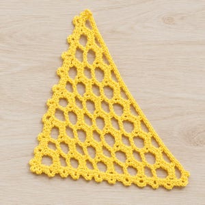 May include: A bright yellow triangular crochet piece featuring an openwork mesh pattern with a repeating hexagonal design. The edges are finished with a small scalloped border, creating a textured and geometric appearance throughout the item.