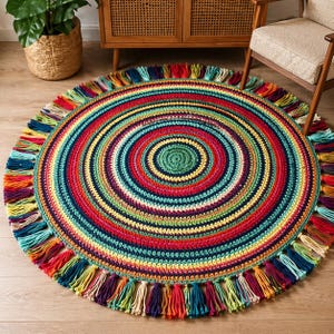 May include: A colourful, circular rug with a spiral pattern in a variety of shades. The rug has a fringed edge with tassels in different colours. The rug is made of yarn and is placed on a wooden floor.