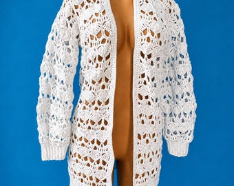 May include: A white long-sleeve cardigan featuring an intricate openwork crochet pattern with a shell-like motif. The garment has a straight open front, long sleeves with ribbed cuffs, and a ribbed hemline, crafted from a lightweight white yarn.