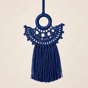 May include: A dark blue macrame ornament featuring a central circular ring wrapped in cord, an intricate fan-shaped crocheted pattern extending outward, and a long, dense fringe of hanging vertical threads suspended from the bottom edge.
