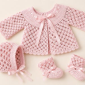 Peut inclure: Ensemble de bébé au crochet rose clair. Il comprend une veste avec un nœud en ruban, un bonnet et deux chaussons. Le motif ajouré est rehaussé de rubans de satin, pour un look délicat.