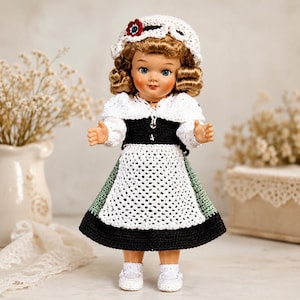 May include: A doll with curly blonde hair wearing a white crocheted bonnet with a red and blue flower, a white crocheted shawl, a black bodice, a white crocheted apron, a green and black skirt, and white crocheted shoes with small buttons.